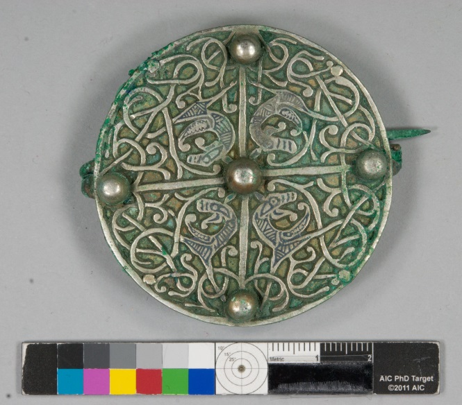 A circular brooch densely decorated with interlaced vines and four enigmatic beasts, one in each of the brooch's four quadrants. The brooch is tinted green with age.